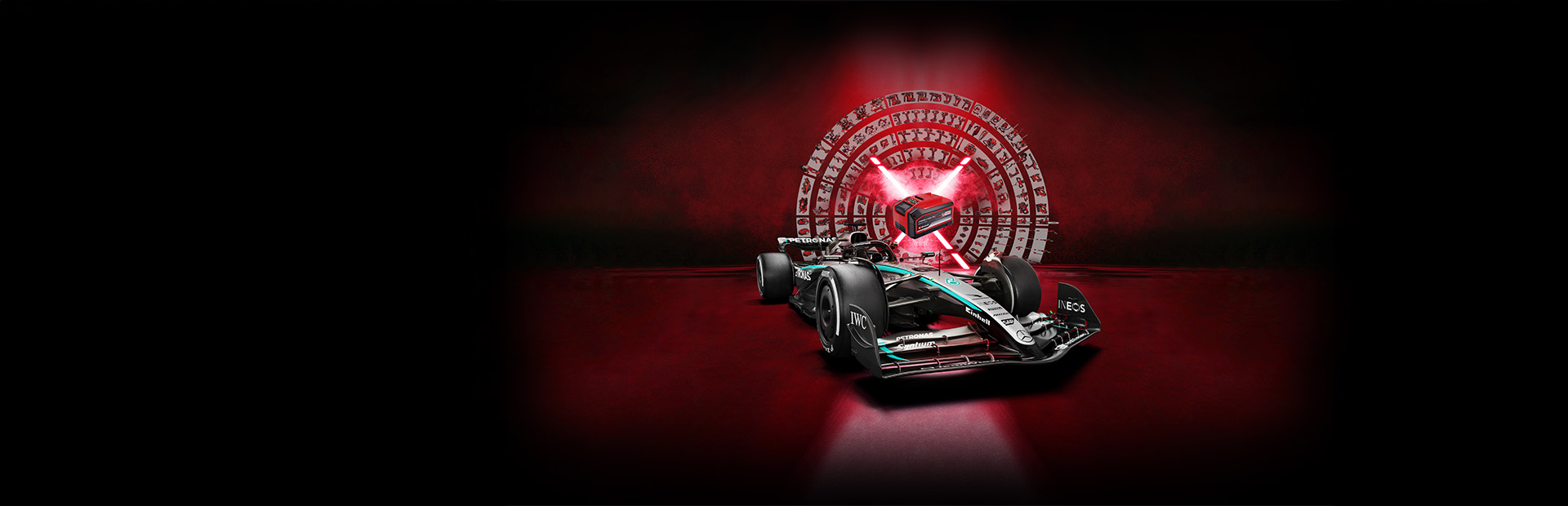 Un carro de carreras de Fórmula 1 Mercedes-AMG PETRONAS frente a un fondo rojo con una batería Einhell Power X-Change al centro iluminada por haces de luz rojos.