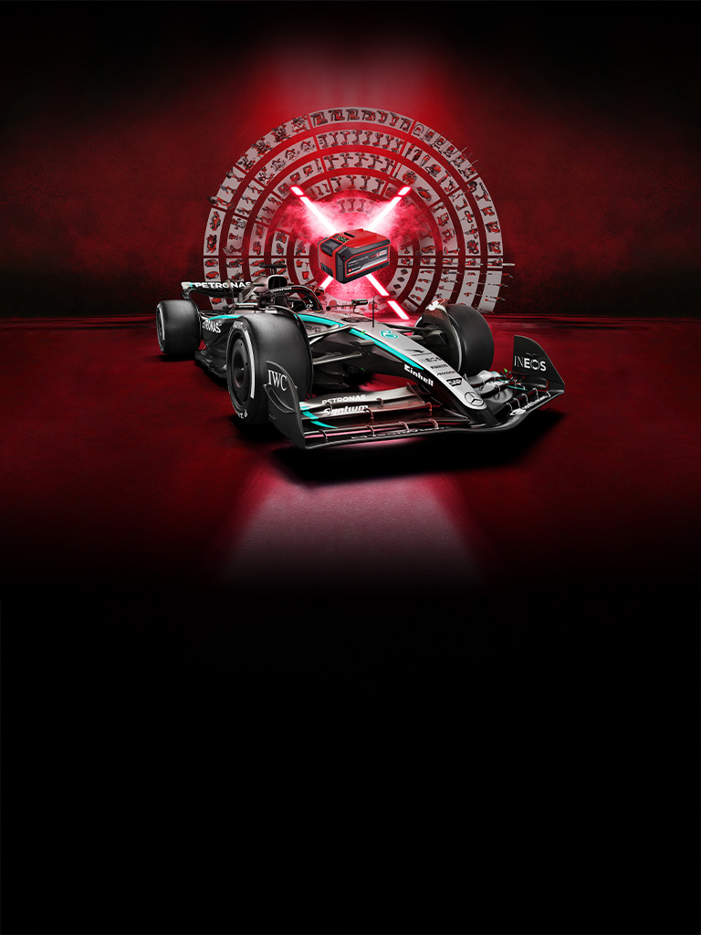 Un carro de carreras de Fórmula 1 Mercedes-AMG PETRONAS frente a un fondo rojo con una batería Einhell Power X-Change al centro iluminada por haces de luz rojos.
