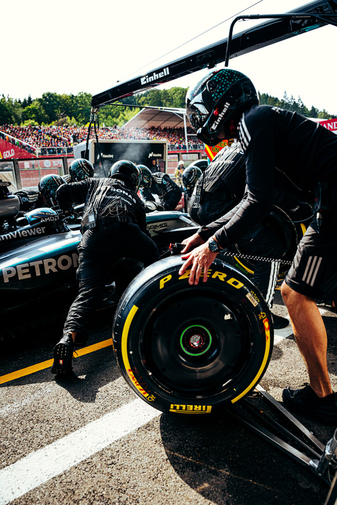 Los mecánicos del equipo Mercedes-AMG PETRONAS Formula One Team realizan una parada en boxes. Uno de los integrantes prepara una llanta Pirelli mientras los demás trabajan en el auto. El logo de Einhell es visible en el equipo que está encima del vehículo.