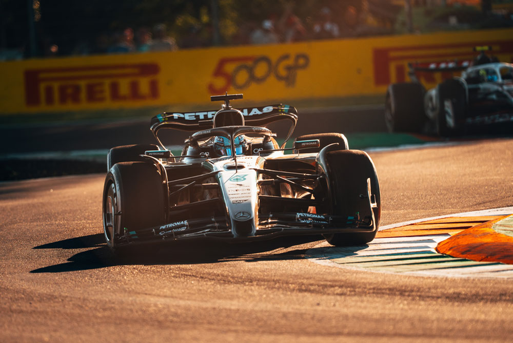 Un auto del equipo Mercedes-AMG PETRONAS Formula One corre en una pista soleada durante un Gran Premio. El vehículo toma una curva a gran velocidad, mientras otro auto se ve al fondo.