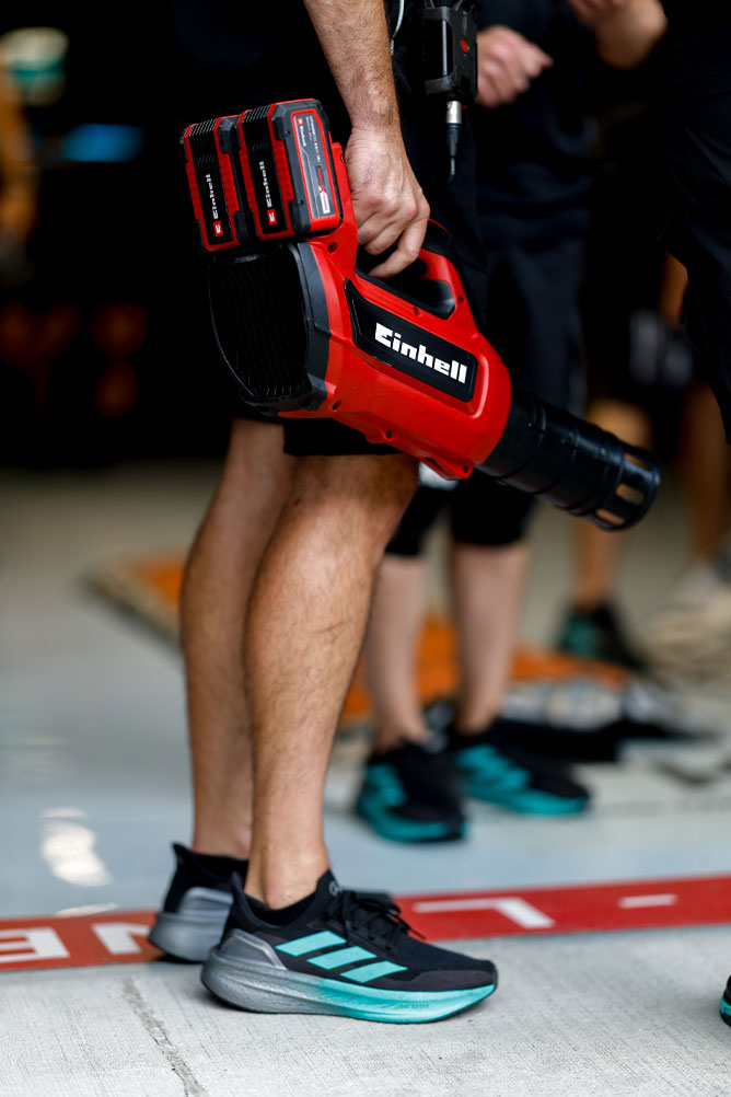 Un integrante del equipo sostiene una sopladora inalámbrica roja de Einhell con dos baterías Power X-Change. La escena ocurre en la zona de boxes durante un evento de Fórmula 1.