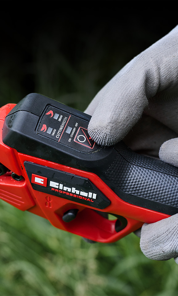 Primer plano de un dispositivo inalámbrico rojo de Einhell con una mano enguantada ajustando su modo.